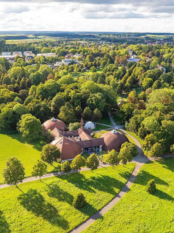 Historic ensemble of buildings with reddish-brown roofs surrounded by lush parkland under a cloudy sky, Bad Dürrheim, Germany