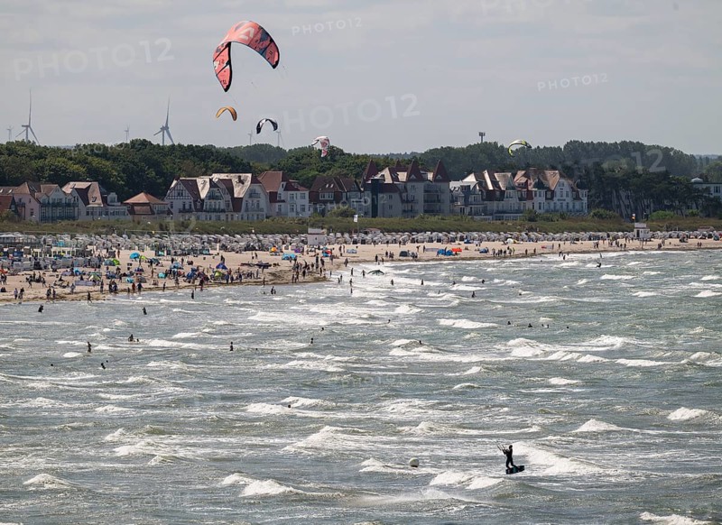 Kitesurfers and holidaymakers on the beach and in the sea, waves, beach chairs, houses in the background, Warnemünde, Rostock, Mecklenburg-Vorpommern, Germany