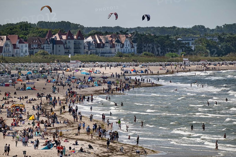 Lively beach with holidaymakers in the sea and on the beach, kite surfers in the surf, Warnemünde, Rostock, Mecklenburg-Vorpommern, Germany