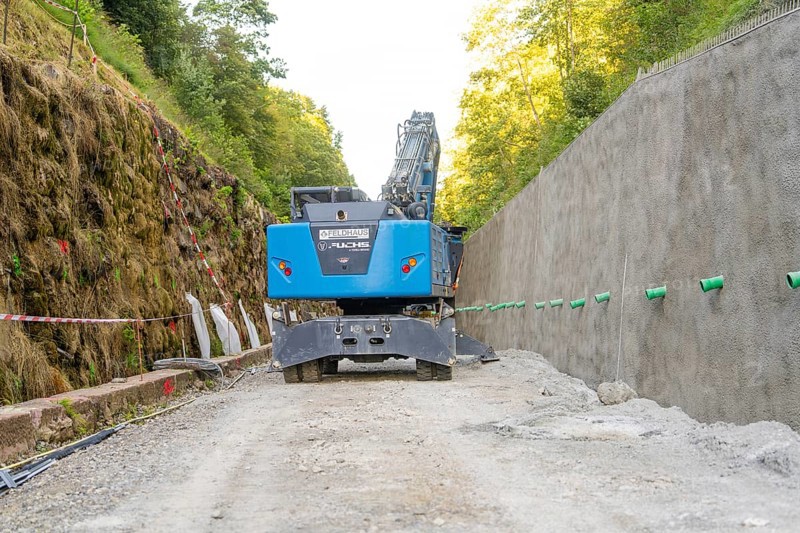 Blue excavator on a construction site between wooded earth slopes, Hermann Hessebahn construction site, Calw, Germany