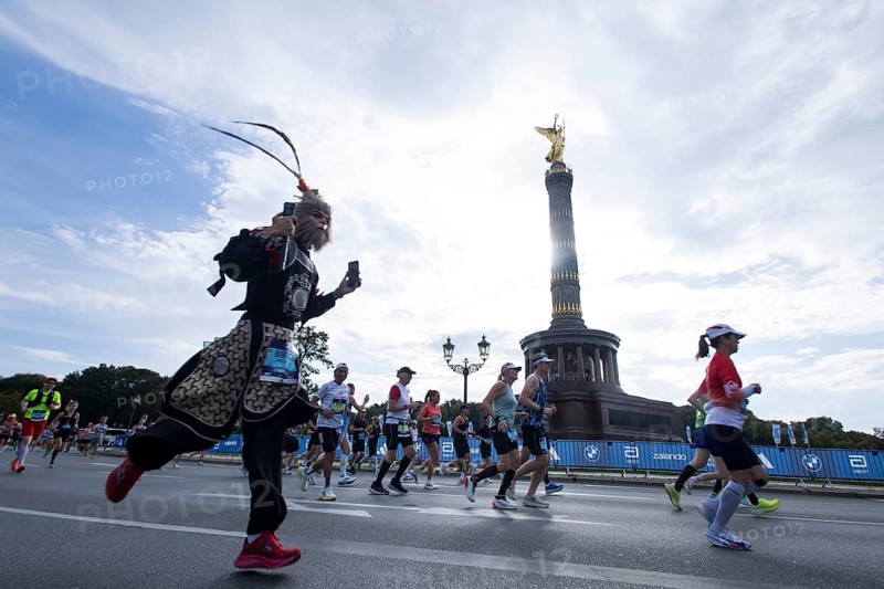 A disguised runner runs around the Victory Column against the backlight of the sun on the Great Star at the 51st BMW Berlin Marathon 2025 on 21 September 2025