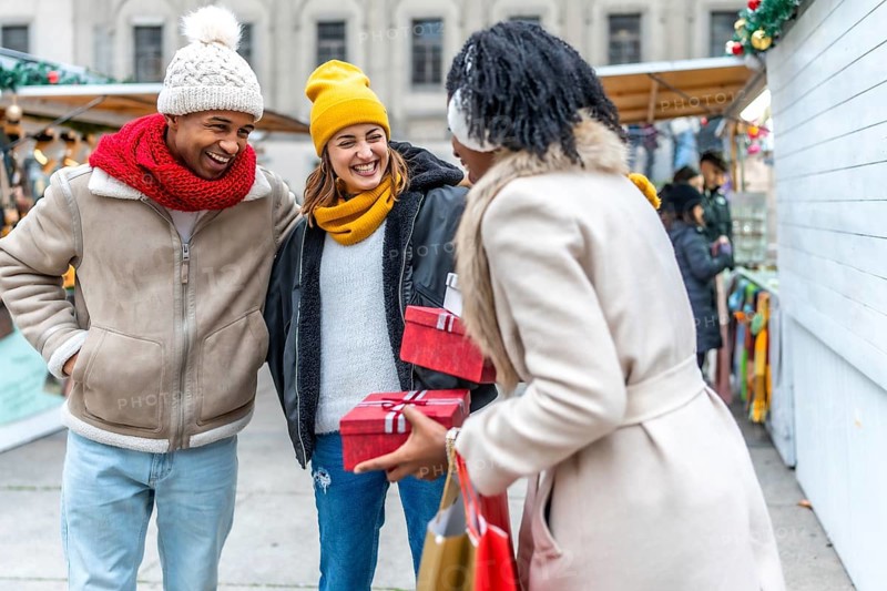 Happy friends exchanging christmas gifts while enjoying a stroll through a festive winter market