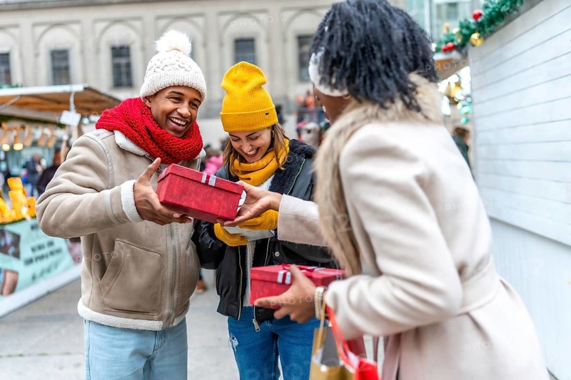 Happy multi ethnic friends exchanging christmas gifts at a christmas market, enjoying winter holidays together