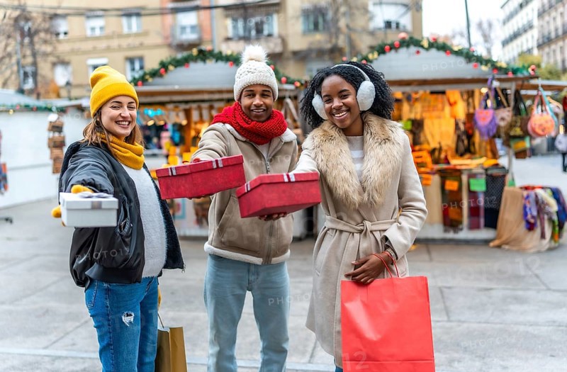 Happy multi ethnic friends showing christmas gifts at a decorated outdoor christmas market