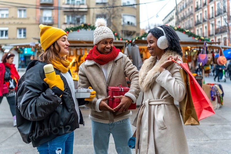 Happy multi ethnic friends exchanging christmas gifts while enjoying a stroll through a winter street market