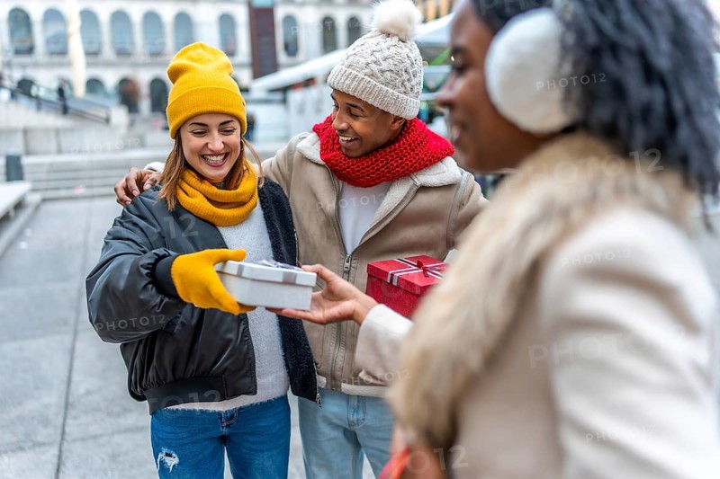 Happy multi ethnic friends joyfully exchanging christmas gifts in a bustling city, celebrating the warmth of friendship during wintertime
