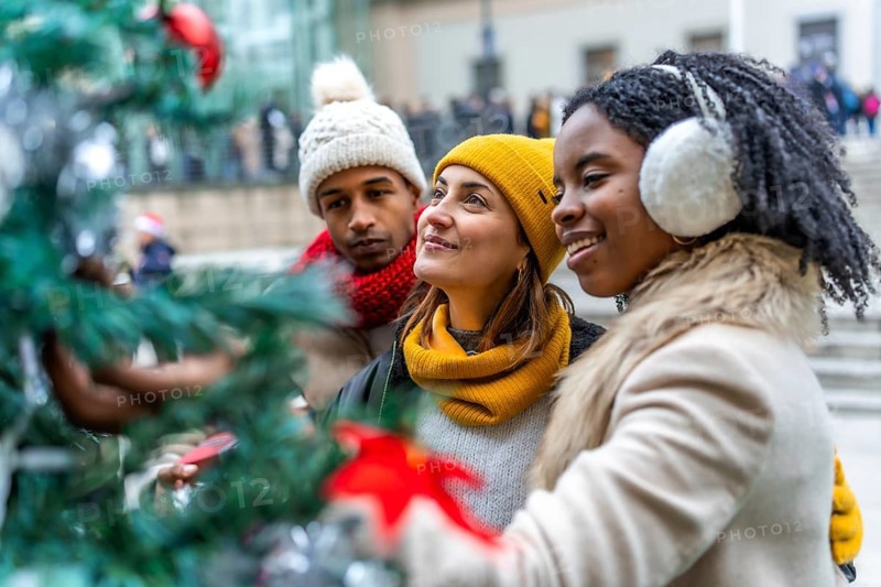 Three friends admiring christmas decorations on a city tree during winter holidays, enjoying time together