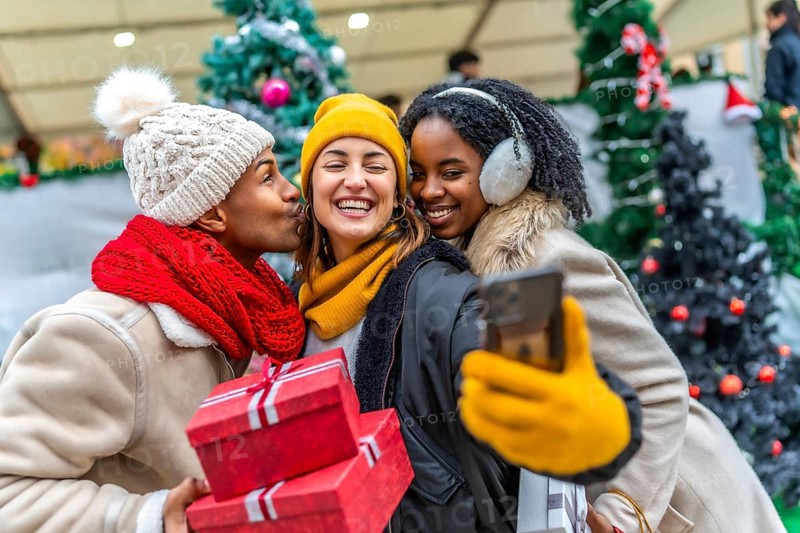 Happy multi ethnic friends taking a selfie at the christmas market, holding gifts and smiling