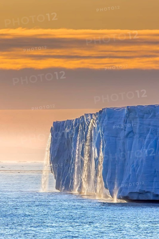 Waterfall at edge of Brasvellbreen glacier from the ice cap Austfonna pouring into the Barents Sea at sunset, Nordaustlandet, Svalbard, Spitsbergen