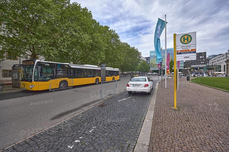 City centre, bus stop Schlossplatz, street, pavement made of cobblestones, public bus, taxi, general architecture, flags on flagpoles, trees, milky blue sky, diffuse light, Königstraße, Stuttgart, state capital, city district Stuttgart, Baden-Württemberg, Germany