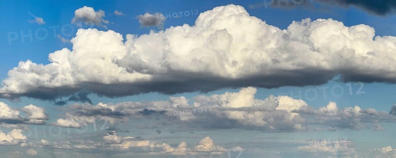 Stratocumulus cloud in the centre of the picture, dense cloud cover of many different cumulus clouds in the background, bright blue sky above, international