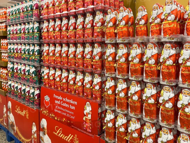 Display in shelf of wholesale of chocolate Santas Father Christmases Chocolate Father Christmases in different colours of staniol paper of chocolate brand Lindt arranged like army of Father Christmas, Germany