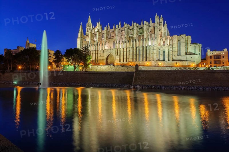 Night shot atmospheric photo in blue hour of Cathedral of Saint Mary of the Holy Mary Episcopal See La Seu, in front artificial lake water basin in Parc de la Mar with fountain fountain reflection on water surface, Palma de Majorca, Majorca, Balearic Islands, Spain
