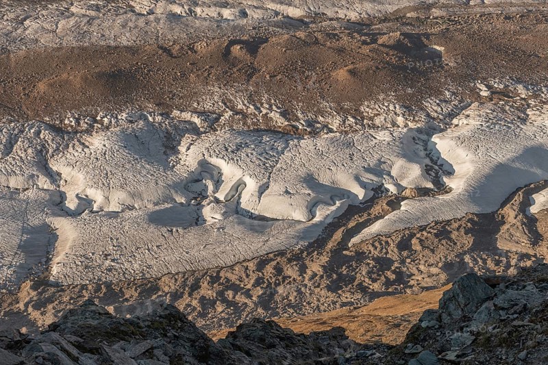 Detailed glacier formations stretch across the rocky landscape, revealing crevasses and structures, while the sunlight illuminates the scenery in the late afternoon. Gorner Glacier, Zermatt, Valais, Alps, Swiss