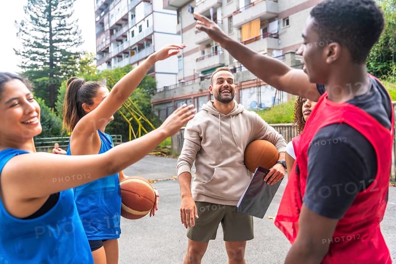 Group of happy basketball players giving high five to their coach after training session on outdoor court, celebrating teamwork and success