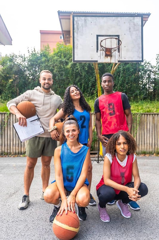 Multi ethnic basketball team posing with their coach on an outdoor court, showcasing teamwork, diversity, and athleticism in a sport setting