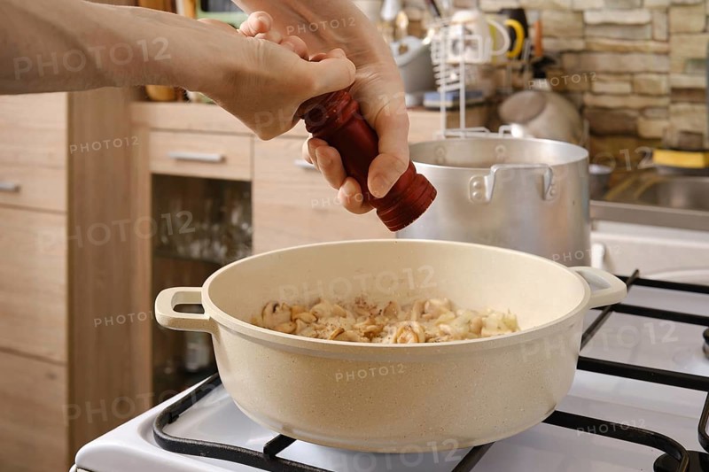 Adding ground pepper in sliced mushrooms roasted in a pot on the stove in the kitchen