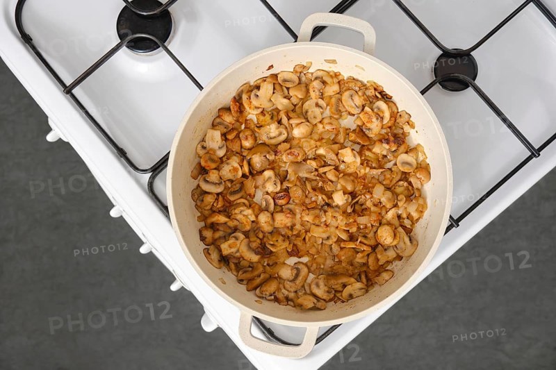 Top view of golden champignon mushrooms fried in oil in a frying pan on the stove in the kitchen