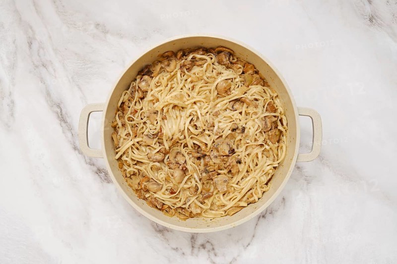 Overhead view of double handled pot with cooked noodles and creamy mushroom sauce on a marble kitchen surface
