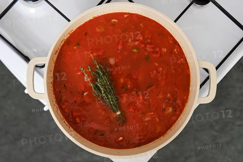 Close-up overhead view of a cast iron pot with tomato and bread soup on a gas stove