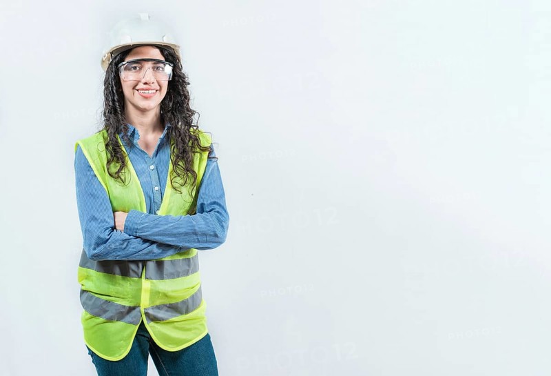 Portrait of smiling female engineer with arms crossed isolated. Young female engineer with helmet and vest looking at camera isolated