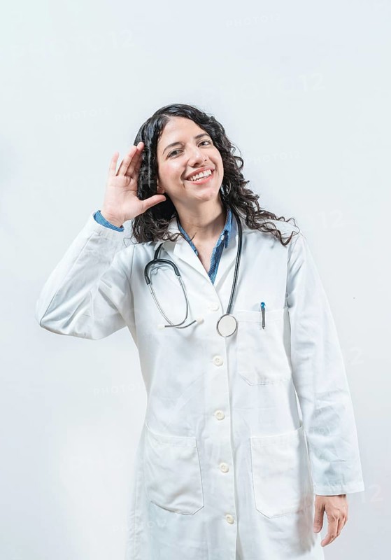 Doctor with hand on ear listening to a rumor, isolated. Latin female doctor hearing a rumor, looking at the camera