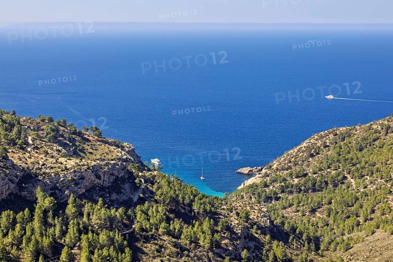 Scenics view at a sea bay with boats from a mountain with green forest and a seascape view to the horizon on the mediterranean sea a sunny summer day, Mallorca, Spain