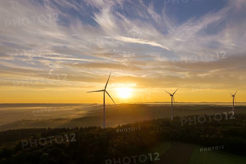 Wind turbines stand still under a soft sunlight illuminating the sky and forest, near Schorndorf, Remstal, Rems-Murr-Kreis, Baden-Württemberg, Germany