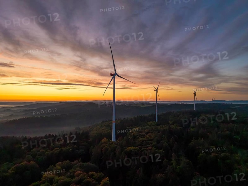 Wind turbines stand in a wooded landscape under a pastel-coloured sky at sunrise, near Schorndorf, Remstal, Rems-Murr-Kreis, Baden-Württemberg, Germany