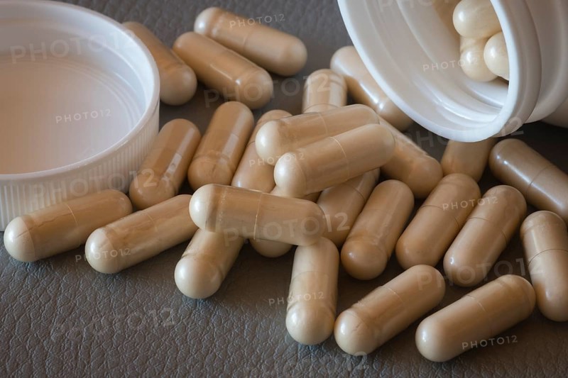 Close-up of beige capsules rolling out of an open bottle onto a surface, food supplement, iron supplement, vitamin supplement