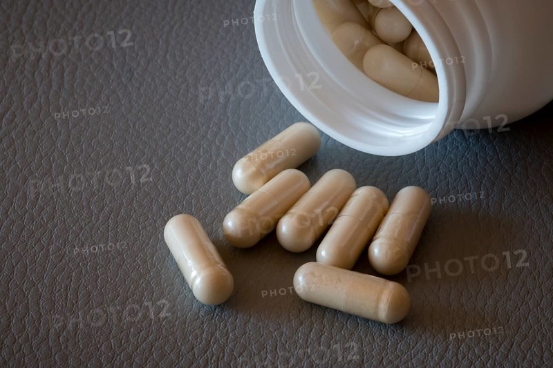 Partially emptied bottle with beige capsules on a textured surface, food supplement, iron supplement, vitamin supplement