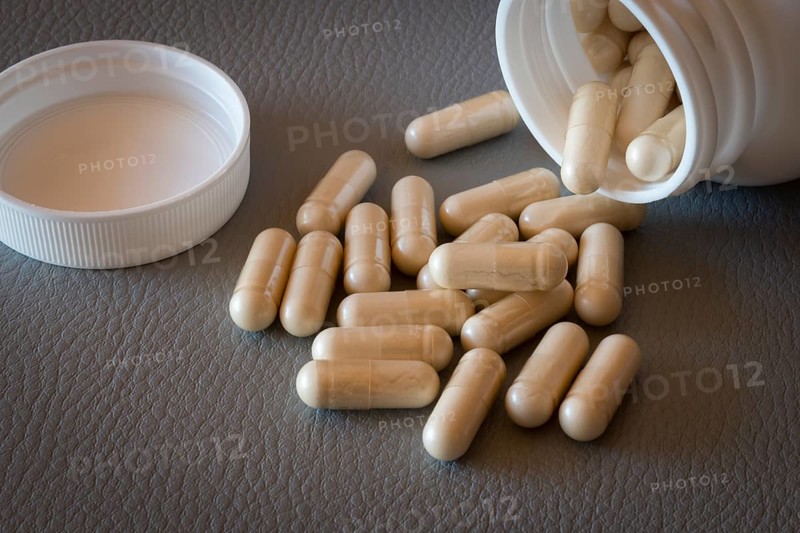 Beige capsules that have fallen from an open bottle with the lid removed onto a surface, food supplement, iron supplement, vitamin supplement