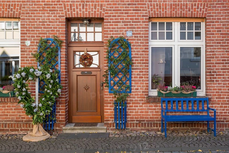 A decorated brick house façade with a blue bench and floral decorations next to the entrance, North Rhine-Westphalia, Germany