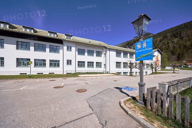 Primary and secondary school Bischofswiesen, sign Stop parent taxi, building, lantern, bus stop, problem parent taxi, wooden fence, hill, coniferous forest, blue sky, cirrostratus clouds, intersection Göllstraße with Schulstraße, Bischofswiesen, district Berchtesgadener Land, Bavaria, Germany