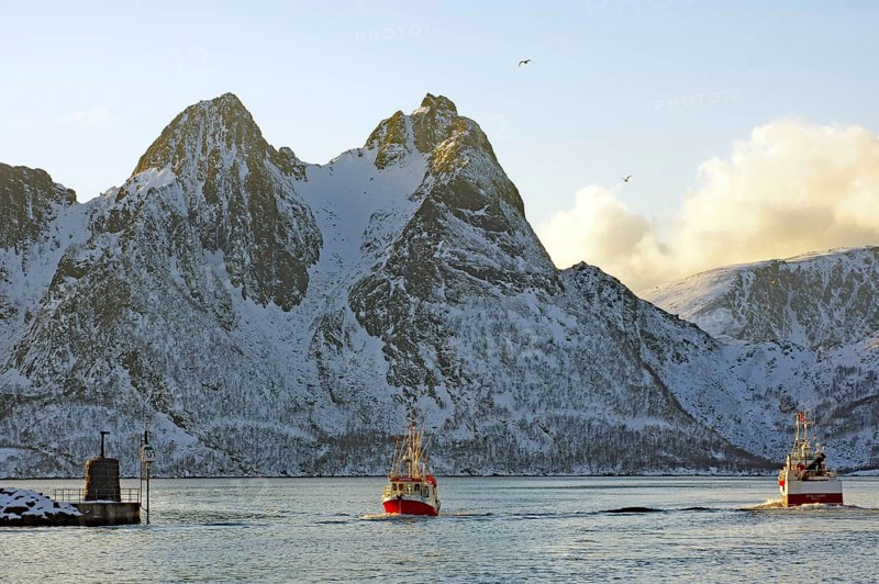 Two fishing boats sailing through the sea in front of snow-covered mountains, Myre, Vesteralen, Nordland, Arctic, Norway