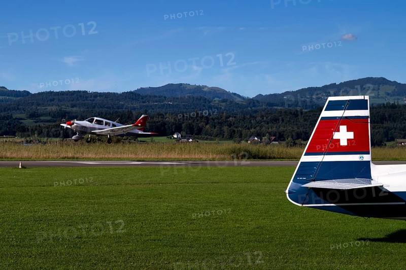 Piper Archer II with the registration HB-PPY on take-off, tail unit of a Mooney M20J 200 HP HB-DGW on the ground, Wangen-Lachen airfield, LSPV, Canton Schwyz, Switzerland