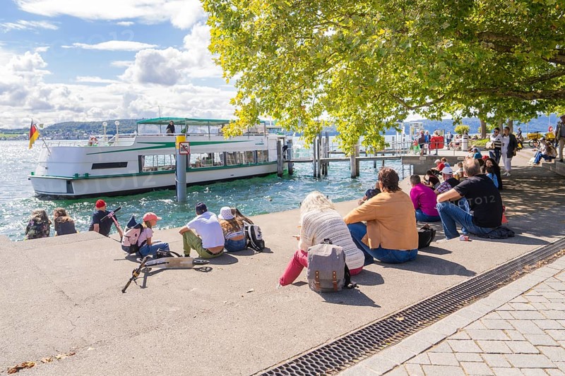 People sitting on the shore of a lake and watching an arriving ship, Lake Constance, Germany