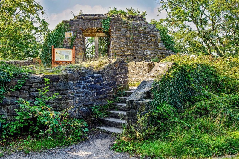 View down old staircase in historic castle courtyard to entrance of former residential building residential wing behind remnant of wall with window niche part of ruins of Isenburg Castle, Schellenberger Wald, Essen, North Rhine-Westphalia, Germany