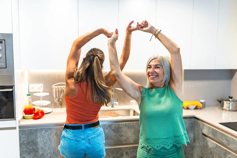 Two women joyfully dancing in a modern kitchen, embodying happiness and togetherness, surrounded by fresh ingredients and bright decor