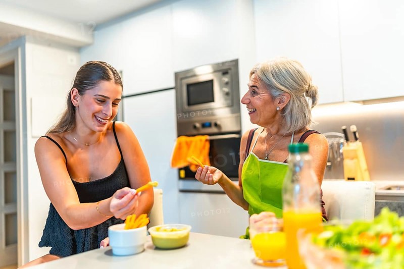 Two women, one older and one younger, enjoying healthy snacks together in a modern kitchen, highlighting family bonding and healthy living