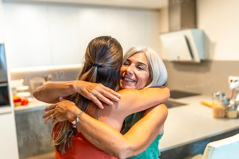 Happy senior woman embracing her adult daughter in a kitchen, enjoying a tender moment of affection and family connection