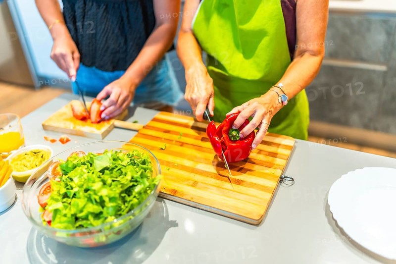 Two chefs are slicing fresh vegetables on wooden cutting boards, preparing ingredients for a healthy salad in a bright, modern kitchen