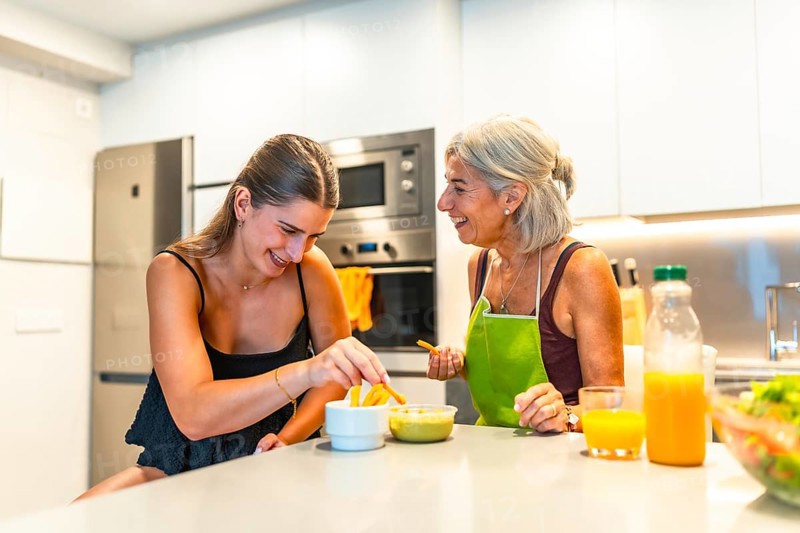 Elderly woman and young woman sharing a joyful moment in a modern kitchen, preparing food and bonding over a meal