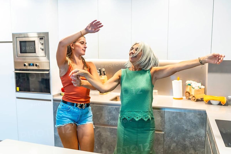 Two women enjoying a lively dance in a sleek, modern kitchen, expressing happiness and energy in a bright, contemporary home setting