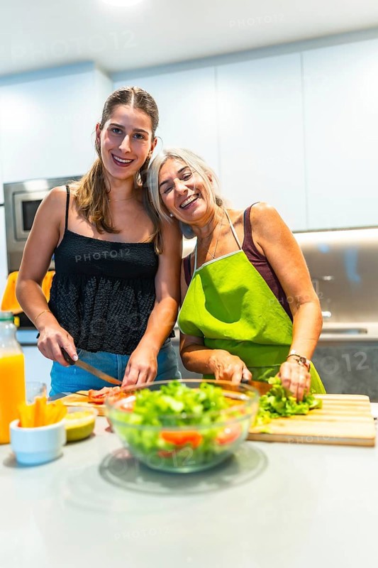 Two women happily preparing a fresh salad in a brightly lit kitchen, showcasing the joy of cooking and healthy living together