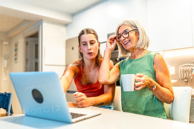 Happy mother and daughter enjoying online streaming content on a laptop while having a coffee in a modern kitchen