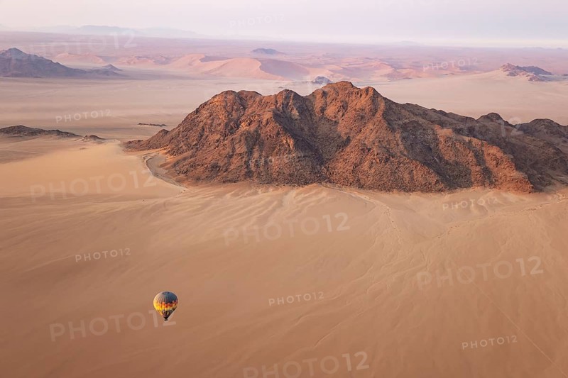 The hot-air balloon above an arid plain and isolated mountain ridges at the edge of the Namib Desert. Aerial view from a second balloon. Namibia