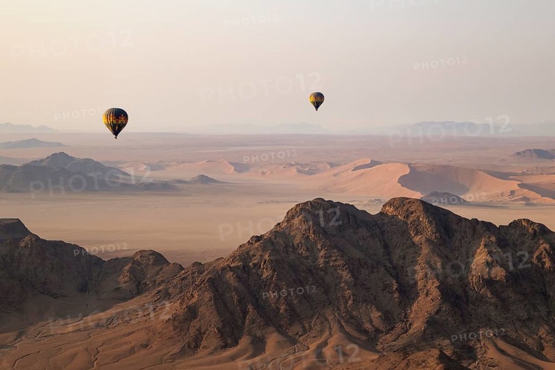 Two hot-air balloons above an arid plain and isolated mountain ridges at the edge of the Namib Desert. Aerial view from another balloon. Namibia