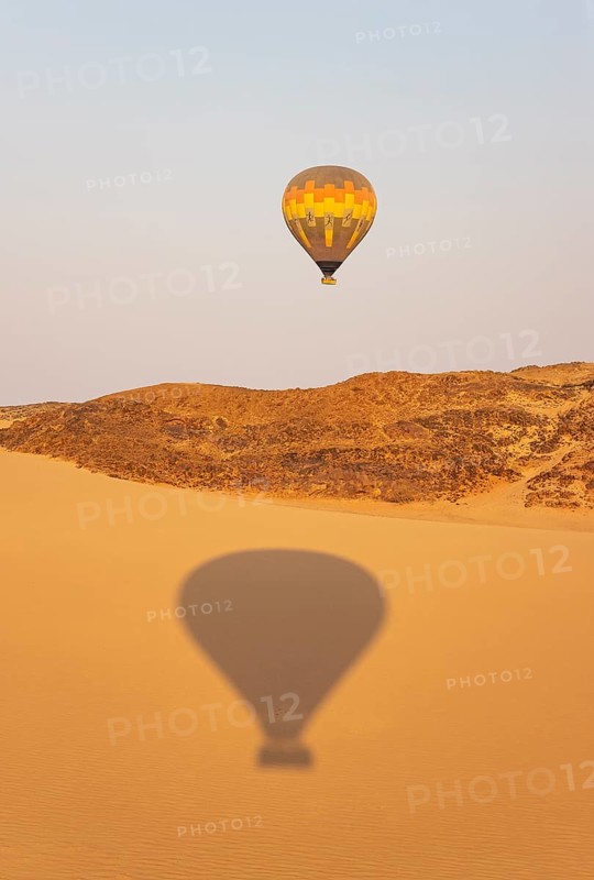 The hot-air balloon above an arid plain and isolated mountain ridges at the edge of the Namib Desert. The shadow is from a second balloon. Aerial view. Namibia