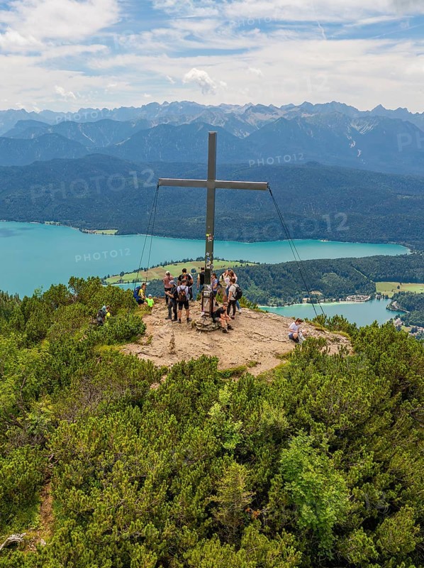 People standing around a summit cross with a view of the surrounding landscape, Herzogstand summit, Walchensee, Schlehdorf, Germany